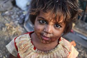 Portrait of the poor child in colorful clothing, with the dirt on the face