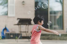 cheerful kid with soap bubbles on the street