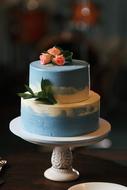 blue and white cake with roses at top on vintage stand