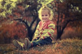 Portrait of a smiling, blonde girl, sitting on the beautiful and colorful hill, among the trees