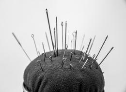 Black and white photo of the shiny sewing needles on the cushion for sewing