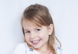 Portrait of the cute, smiling, blonde child girl, near the white wall