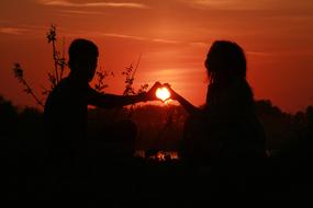 silhouettes of couples with the sun in their hands at sunset