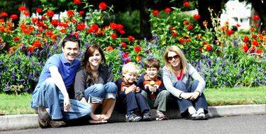 Smiling family, sitting on the road, near the colorful and beautiful plants with flowers