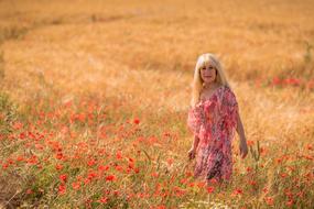 Blonde woman in the colorful dress, among the beautiful, red poppies on the colorful field
