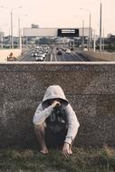young man in hoodie drinks from bottle at road
