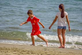 Boy and girl children, playing on the sandy beach, near the water, with the waves