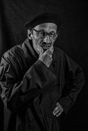 senior man in glasses with hand at mouth, low key Portrait