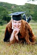 happy redhead girl in Graduation Cap resting on meadow