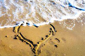 Beautiful heart on the sandy beach with white waves