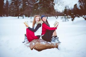 Girls, with the books, sitting on the rock, among the beautiful, snowy forest with the trees, in winter