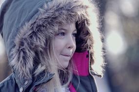 little girl in a warm hood in nature on a blurred background