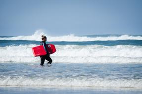 girl with a red board in the waves of the surf on a sunny day