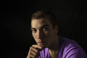photo portrait of a pensive young man in a purple t-shirt at dark