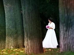 Bride in the white wedding dress, among the beautiful trees, yellow flowers and green grass