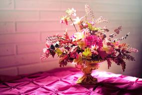Bouquet in golden vase at brick wall