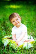 Cute, smiling boy sitting on the beautiful green grass field