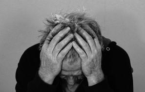Black and white photo of a man, in sadness, holding head with hands