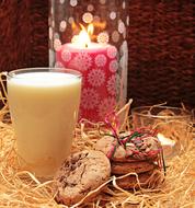 Beautiful and colorful still life with the glass of milk, burning candle and cookies on the hay