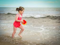 Child Girl with red bucket runs through water