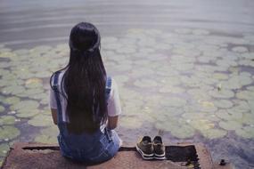 young girl sits on pier at pond
