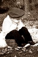 Retro photo of the sitting child in cap, near the fence