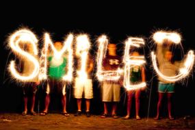 People holding bright "SMILE" sign, at night