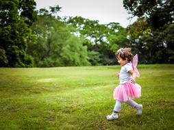 Cute girl in colorful princess costume, walking on the lawn, among the green trees