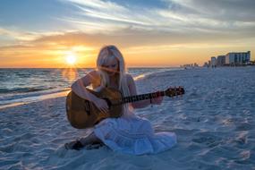 blonde girl with guitar on the beach at dusk