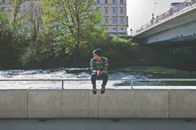 man sits on a concrete fence near the water