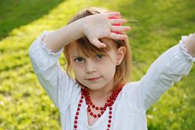 Cute girl in white clothing and with red necklace, on the green grass