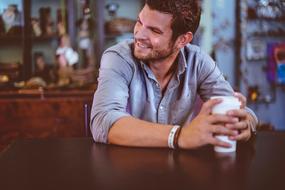 happy young Man wit Coffee cup in hands sits at table