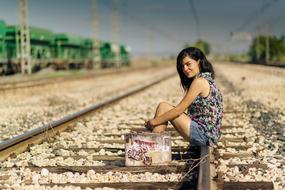 Woman with colorful suitcase sitting on a railway