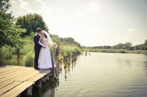 Wedding couple kissing on wooden pier at water