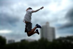 Jumping child, at background with the buildings, under the cloudy sky