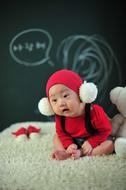 Cute child in red and white clothing, on the soft surface