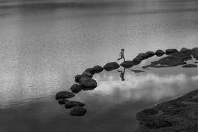 child jumping on large rocks on the water