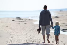 Back view of the father with the child, on the sandy beach, in sunlight