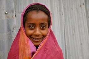 Portrait of the smiling girl, covered in colorful cloth, near the wall