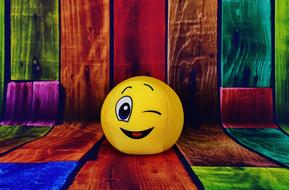 Yellow, winking smiley, on the colorful wooden surface, near the colorful, wooden wall, on clipart