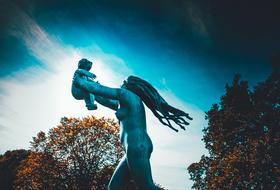 Beautiful statue of the mother with the child, among the colorful trees in the park in Oslo, Norway
