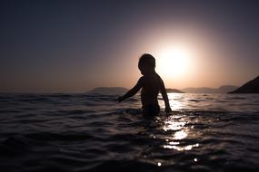 boy swims in the ocean at sunset