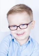 Portrait of the smiling boy child with glasses, in blue shirt, at white background