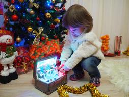 small child Girl opens gift box near christmas tree