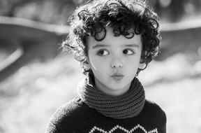 portrait of a curly-haired boy on a blurred black and white background