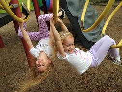 Smiling, blonde girls playing on the colorful playground with equipment