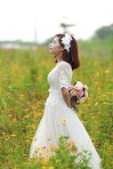 Woman in white wedding dress, with beautiful and colorful flower bouquet, on the field with flowers