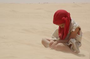 a child in a red scarf on the sand in the desert