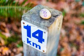 Close-up of the pole with blue and white "14 km" sign on the pole with stone with "hi 5" sign, above the colorful plants
