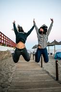 two happy asian girls jump over boardwalk on beach